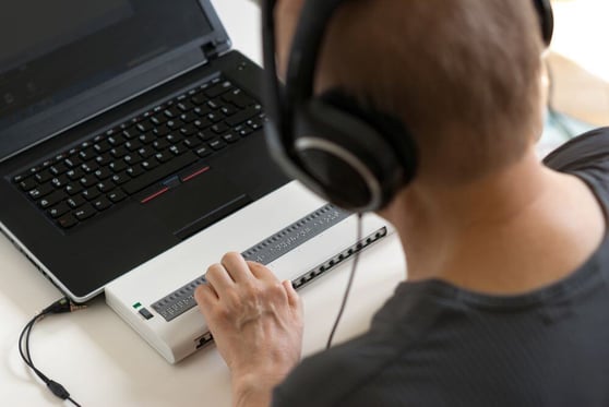 Blind person working on computer with braille display and screen.