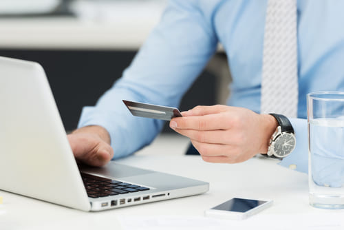 Man holding credit card while browsing his laptop.